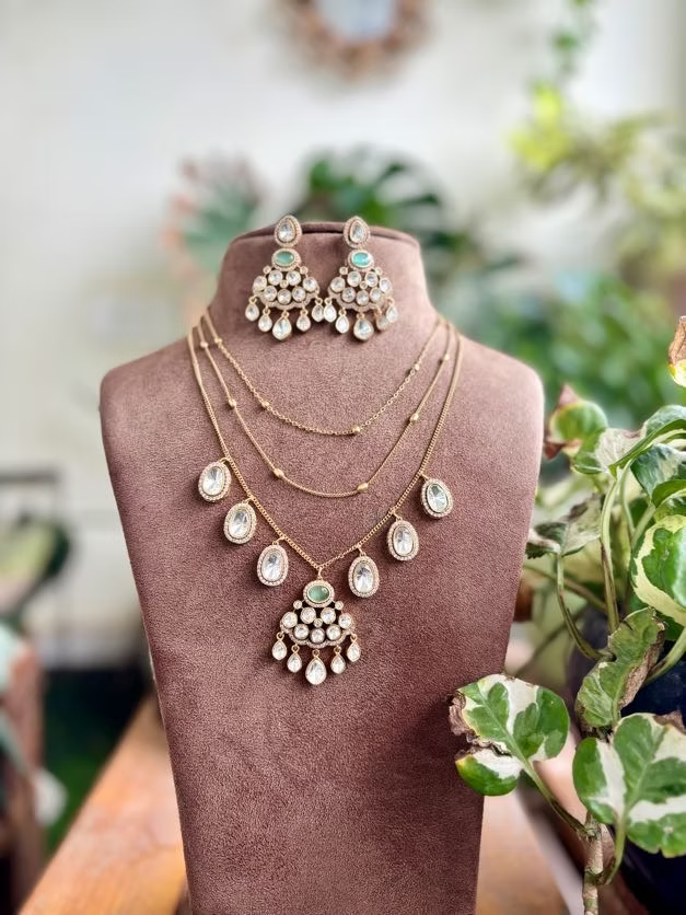 Jewelry set including necklaces and earrings on a mannequin bust with a blurred natural background